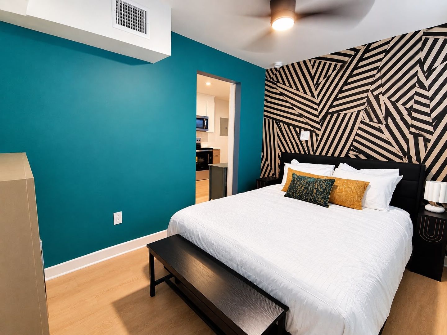 Une chambre moderne avec un mur de couleur turquoise, une tête de lit à motifs, un lit avec une literie blanche et un banc.
