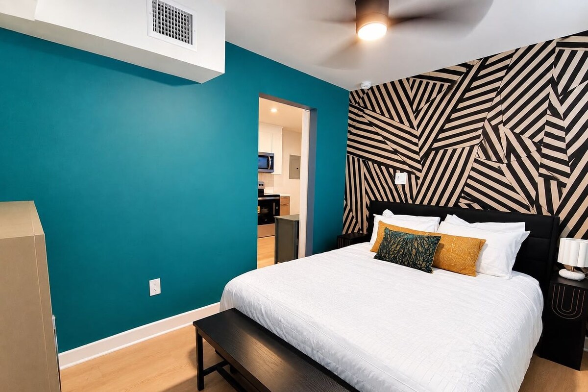 A modern bedroom with a teal wall, a patterned headboard, a bed with white bedding, and a bench.