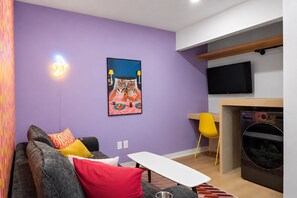 A modern living room with a sofa, a small table, a flat-screen TV, and a painting on the wall. - The Montage (Houston)