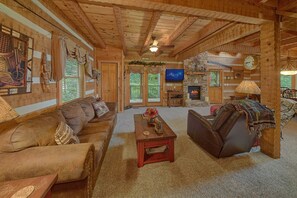 L’intérieur d’un chalet confortable, avec des murs en rondins de bois, un plafond en bois, une cheminée, un téléviseur et un coin salon accueillant.