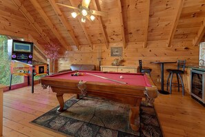 A wooden interior with a pool table, a ceiling fan, and a small table with chairs.