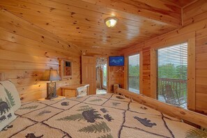 A wooden cabin interior with a bed, a lamp, a television, and a window with blinds. - The Parrots Nest Cabin Rental (Pigeon Forge)