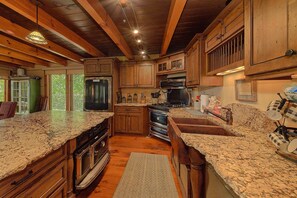 A kitchen with wooden cabinets, granite countertops, a stove, and a refrigerator. - Grouse Ridge Lodge | Smoky Mtn Views, Hot Tub, Sleeps 12, Fire Pit + Free Attraction Tickets (Wears Valley)