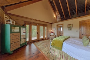 A bedroom with a bed, a dresser, a chair, and a large window with blinds.