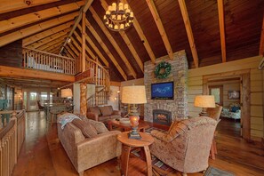 A spacious living room with a fireplace, wooden beams, and a staircase leading to an upper level.
