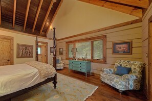 A bedroom with a four-poster bed, a wooden ceiling, a dresser, a chair, and a window with blinds.