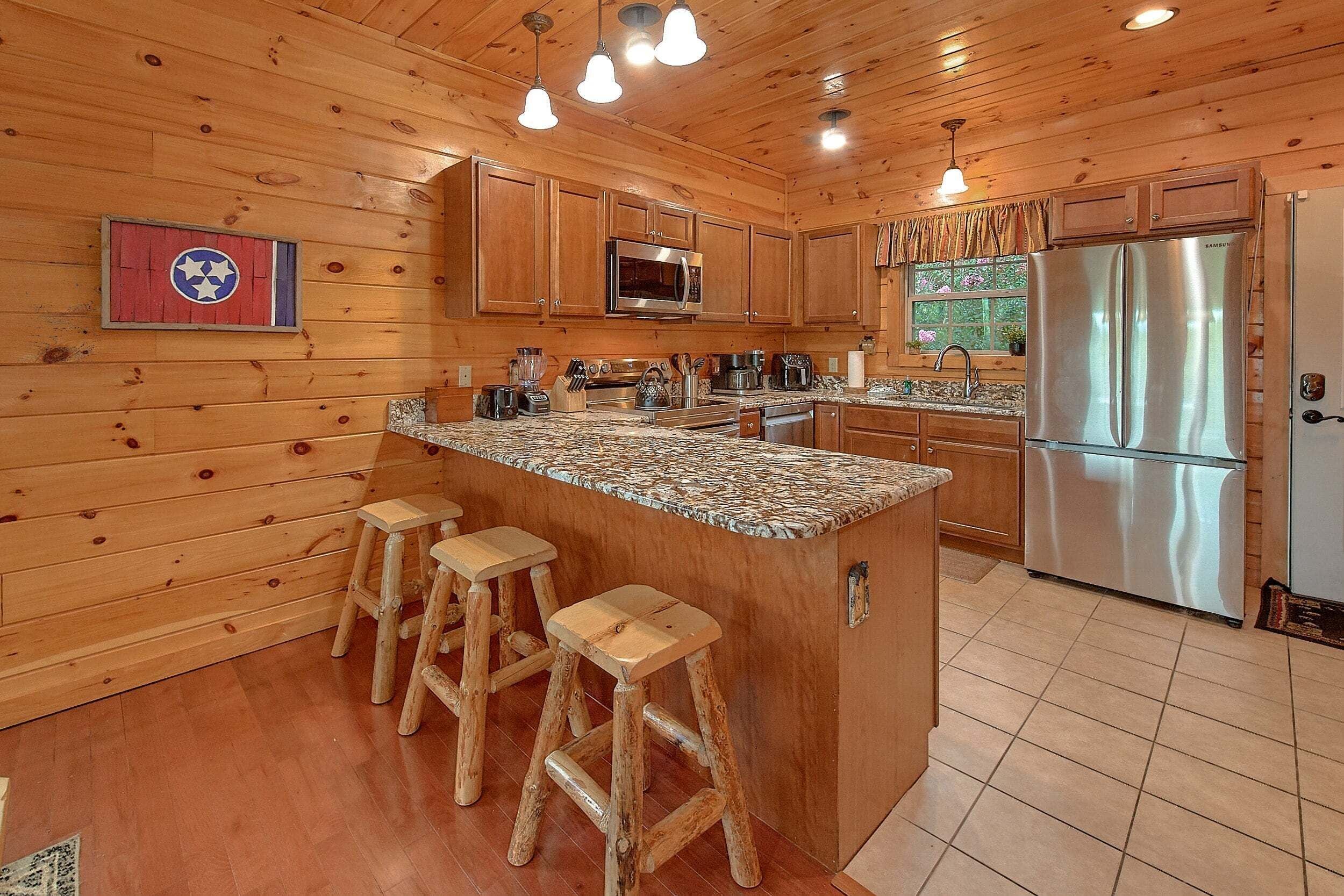 Una cocina con paredes de madera, una isla central con taburetes, electrodomésticos de acero inoxidable y una ventana con cortinas.