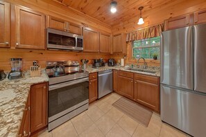 A modern kitchen with wooden cabinets, stainless steel appliances, and a granite countertop. - Almost Heaven II Cabin Rental (Wears Valley)
