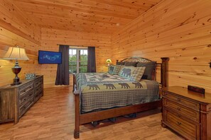 A wooden cabin bedroom with a bed, dresser, and a television on the wall. - Almost Heaven II Cabin Rental (Wears Valley)
