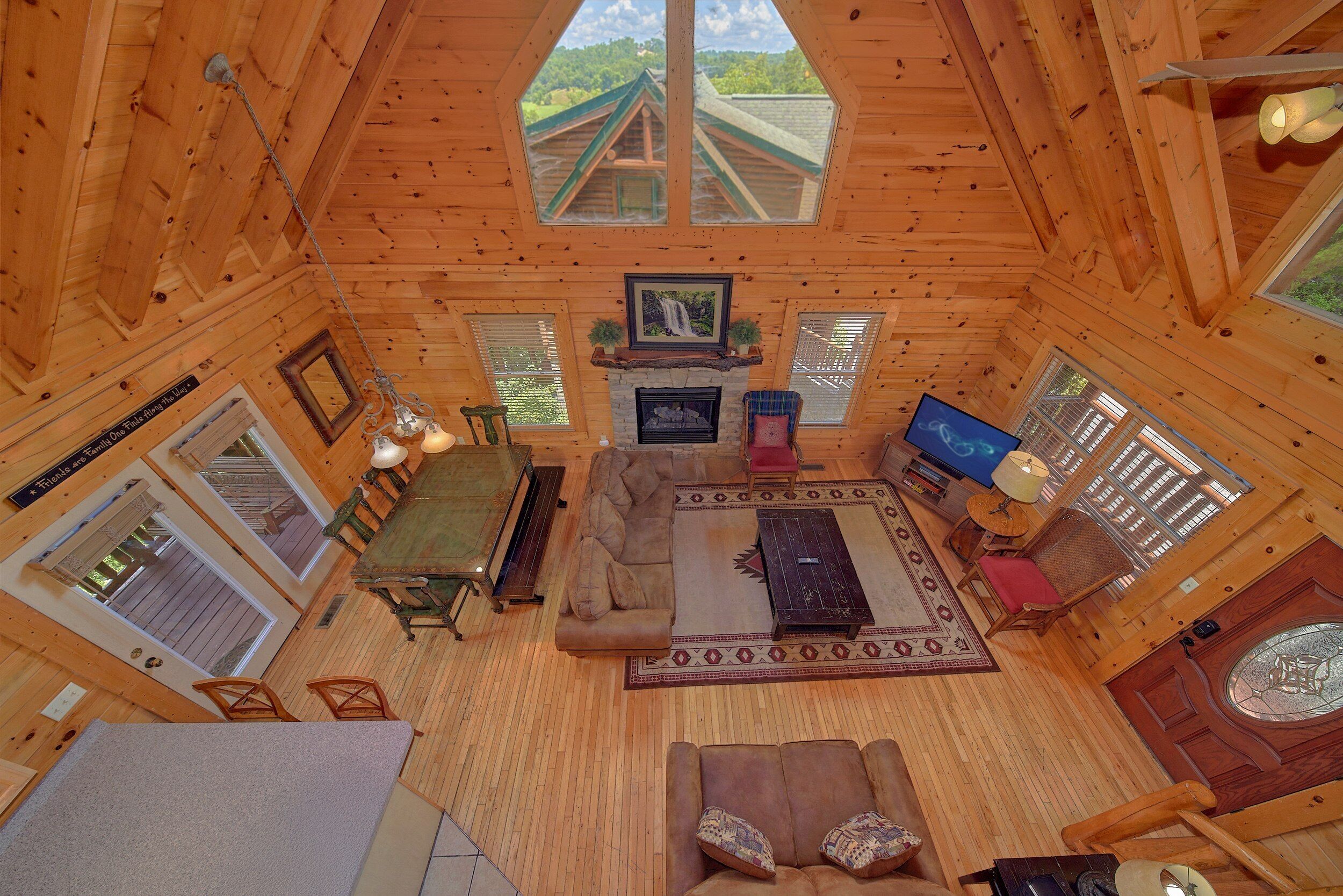 A cozy cabin interior with a dining area, sofa, fireplace, television, and large windows.