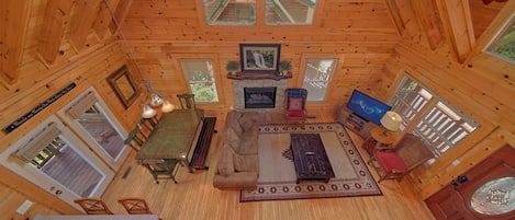 A cozy cabin interior with a dining area, sofa, fireplace, television, and large windows.
