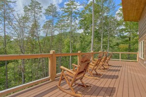 A wooden deck with rocking chairs overlooking a forested area. - Big Bad John's Cabin Rental (Wears Valley)