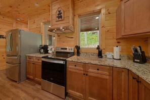 A wooden cabin kitchen with a refrigerator, stove, oven, and granite countertop. - Big Bad John's Cabin Rental (Wears Valley)