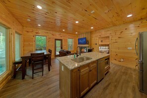 A cabin interior with a kitchen, dining area, and a fireplace. - Big Bad John's Cabin Rental (Wears Valley)