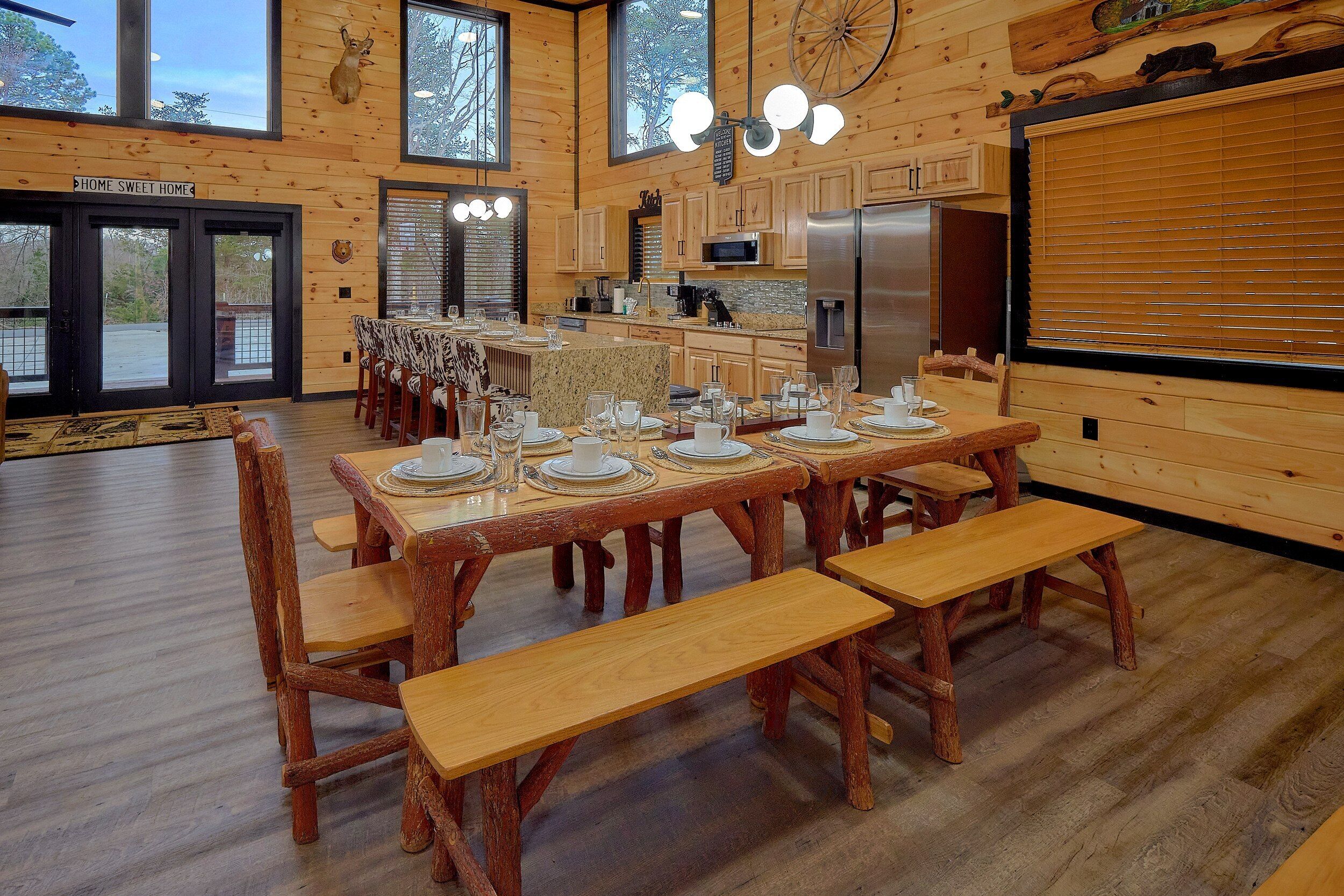 Ein rustikales Holzinterieur mit einem Essbereich, der für eine Mahlzeit gedeckt ist, einer Küche mit modernen Geräten und einem großen Fenster mit Blick auf eine verschneite Landschaft.