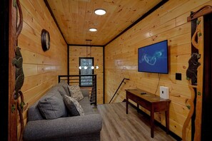 A cozy room with wooden walls, a sofa, a TV, and a window. - Amazing Mountain II Cabin Rental (Sevierville)