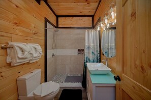 A wooden cabin bathroom with a toilet, shower, and sink. - Amazing Mountain II Cabin Rental (Sevierville)