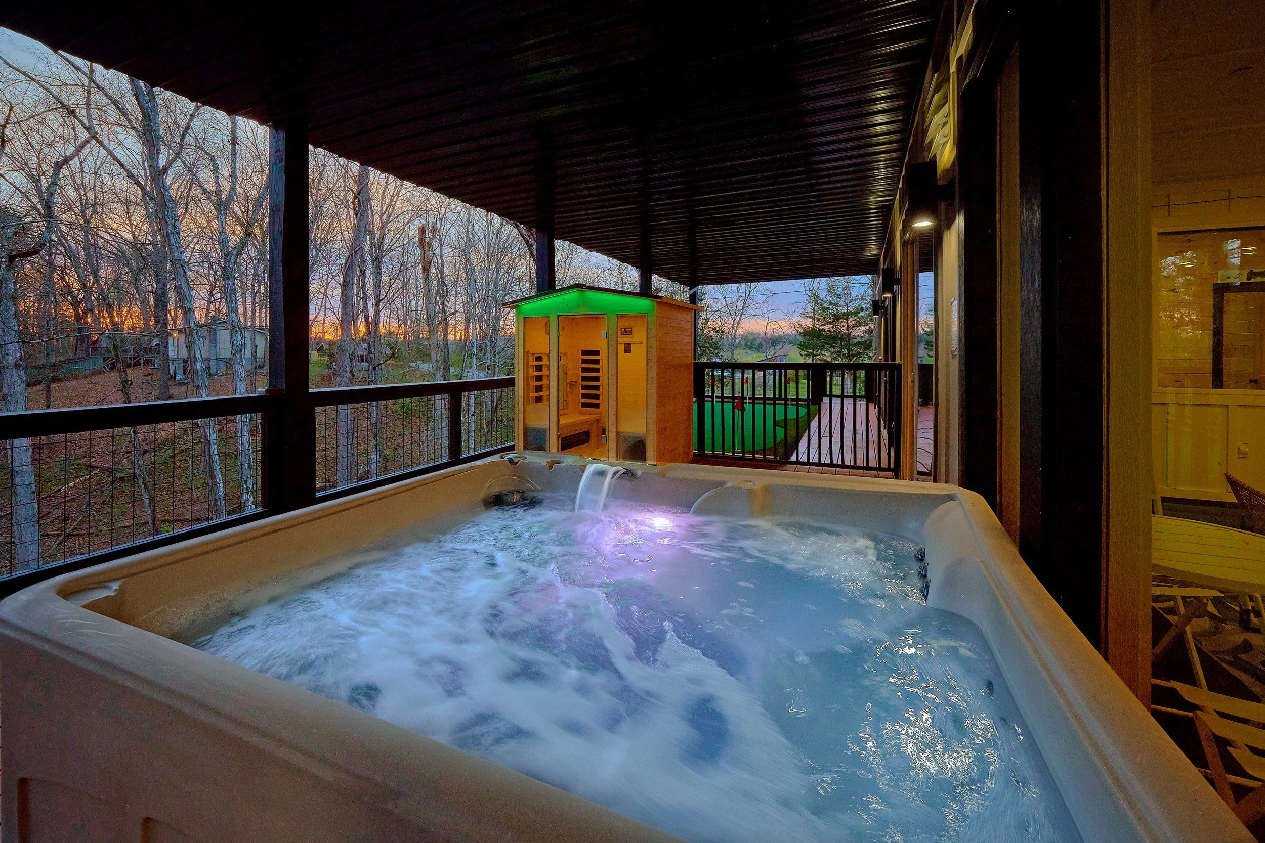 A hot tub with a waterfall feature, surrounded by a wooden deck and a glass enclosure.