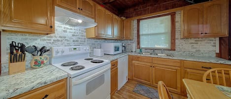 A kitchen with wooden cabinets, a white stove, a microwave, and a sink.