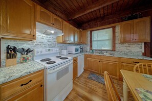 A kitchen with wooden cabinets, a white stove, a microwave, and a sink. - Above the Clouds | Hot Tub | Pool Table | Wi-fi (Pigeon Forge)