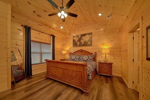 Ein Schlafzimmer mit Holzwänden, einem Bett, zwei Nachttischlampen, einem Deckenventilator und einem Gemälde an der Wand.