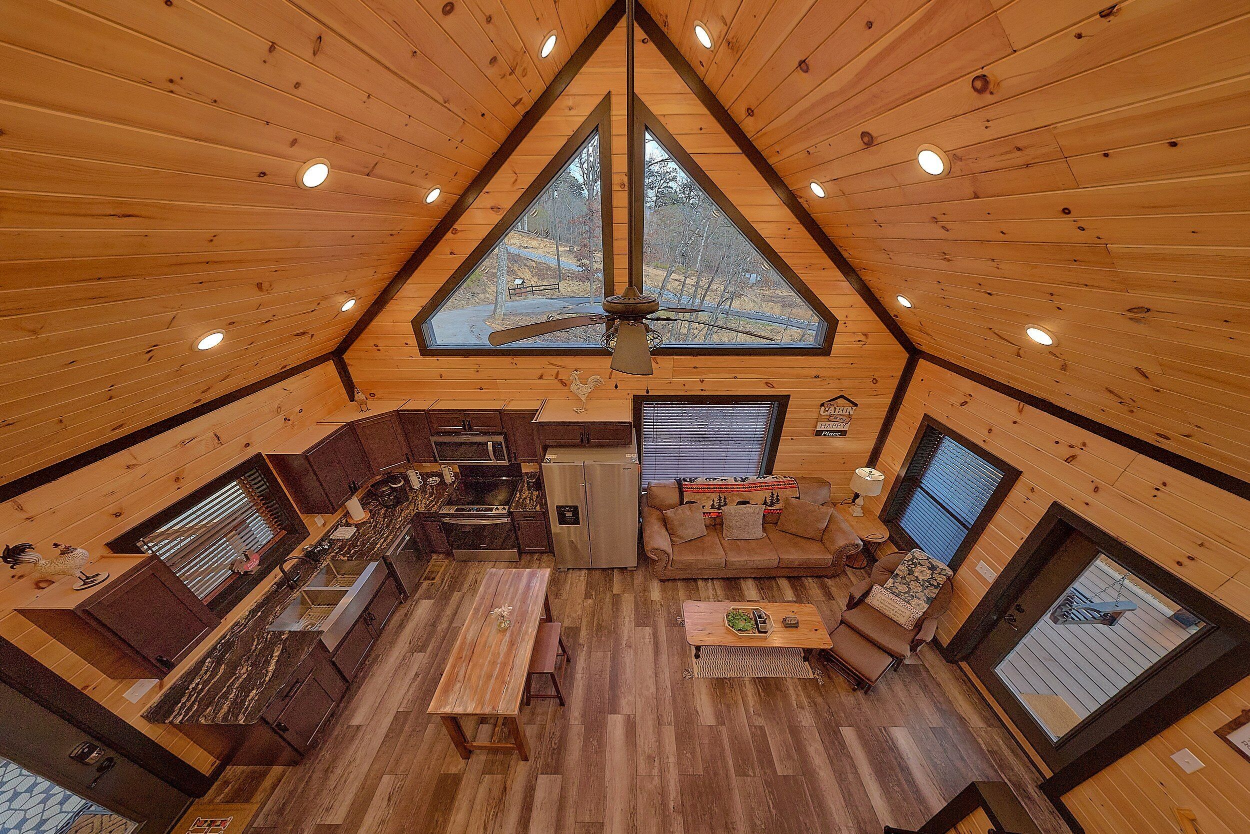 Une cabane dotée d’un toit triangulaire, d’un coin cuisine, d’un espace repas et d’un coin salon offrant une vue sur l’extérieur.