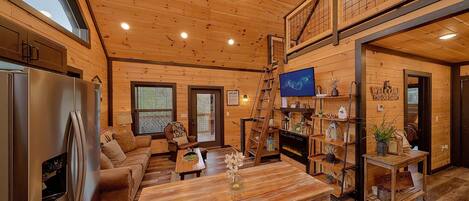 Ein geräumiges Wohnzimmer mit Holzbalkendecke, Kamin, Esstisch und einer Couch.