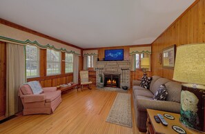 A cozy living room with a fireplace, wooden walls, and a television. - Aspen House Walk to Downtown Gatlinburg River View + Free Attraction Tickets (Gatlinburg)