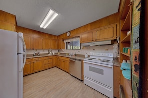 A kitchen with wooden cabinets, a white refrigerator, a stove, and a window above the sink. - Aspen House Walk to Downtown Gatlinburg River View + Free Attraction Tickets (Gatlinburg)