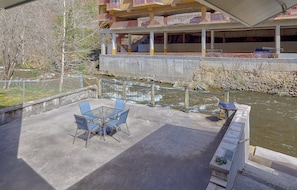 An outdoor patio with a table and chairs, overlooking a river and a building with balconies. - Aspen House Walk to Downtown Gatlinburg River View + Free Attraction Tickets (Gatlinburg)