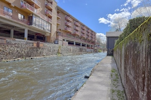 A multi-story building with balconies, a stone wall, and a river. - Aspen House Walk to Downtown Gatlinburg River View + Free Attraction Tickets (Gatlinburg)