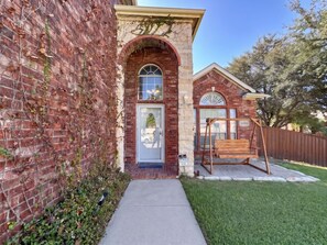 A brick house with a front door, a swing set, and a small garden. - FW Monthly +  Utilities + Laundry + Comfy Stay (Fort Worth)