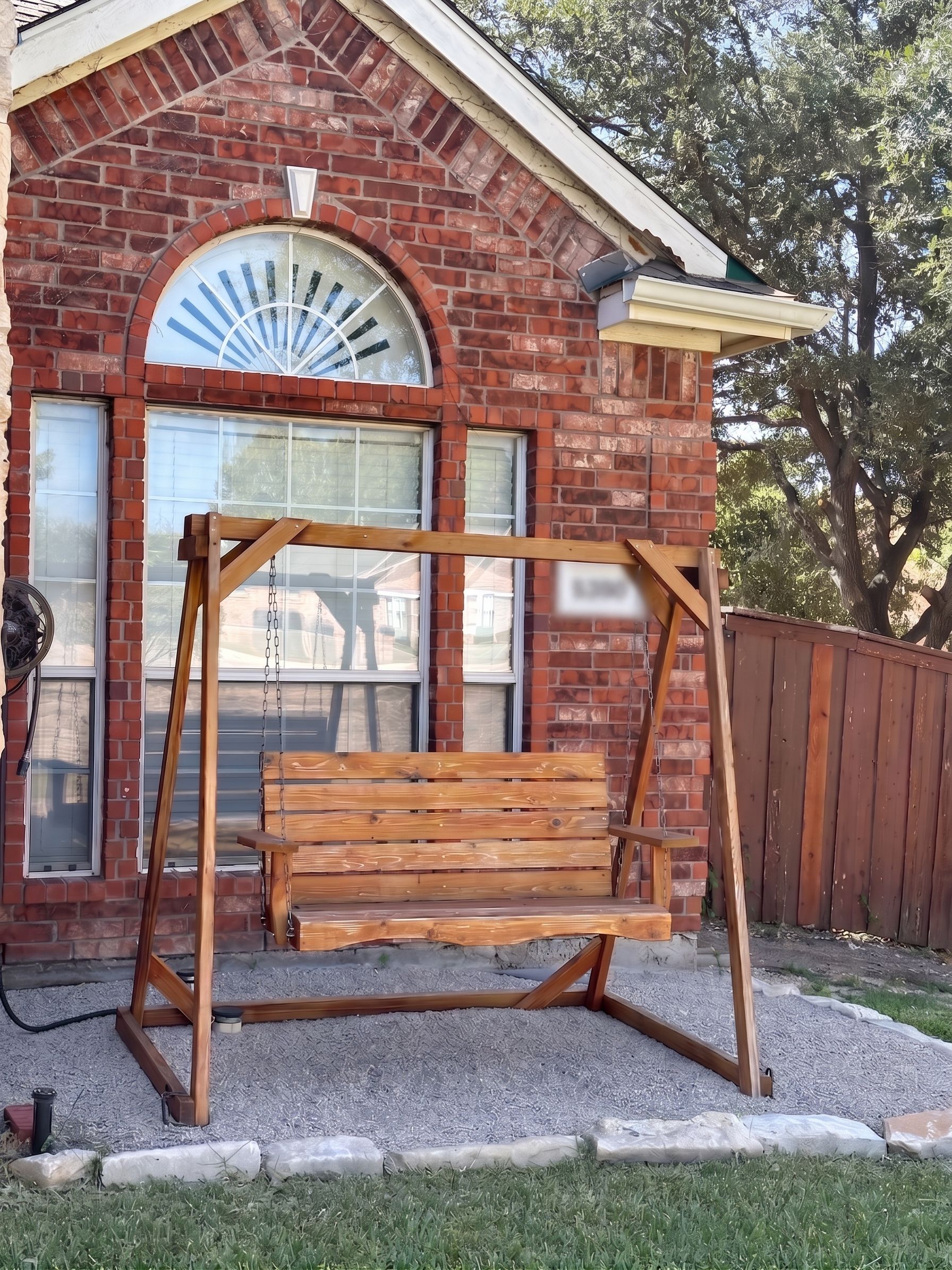A wooden swing set in front of a brick house with a garage door and a large window.