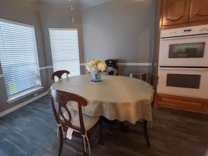 A dining area with a round table, chairs, a vase with flowers, and a kitchen with appliances. - FW Monthly +  Utilities + Laundry + Comfy Stay (Fort Worth)