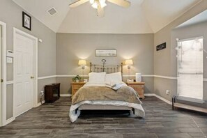 A bedroom with a bed, bedside lamps, a ceiling fan, a window with blinds, and a door. - FW Monthly +  Utilities + Laundry + Comfy Stay (Fort Worth)