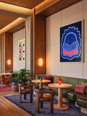 Ein stilvoller Lounge-Bereich mit Holzböden, grünen Polstersitzgelegenheiten und runden Tischen.