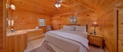 A wooden cabin bedroom with a bed, nightstand, lamp, and a ceiling fan.