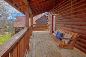 A wooden cabin with a porch, a bench with cushions, and a view of the surrounding landscape. - Autumn Ridge | Hot Tub | Pool Table | Fireplace (Sevierville)