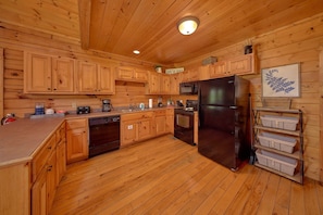 A wooden cabin-style kitchen with wooden cabinets, a black refrigerator, a microwave, a dishwasher, and a coffee maker. - Autumn Ridge | Hot Tub | Pool Table | Fireplace (Sevierville)