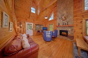 A wooden cabin interior with a leather sofa, two blue armchairs, a fireplace, and a stone wall. - Autumn Ridge | Hot Tub | Pool Table | Fireplace (Sevierville)