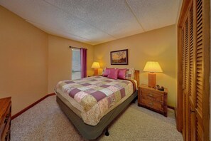 A bedroom with a bed, two bedside tables with lamps, a window with blinds, a painting on the wall, and a wooden wardrobe. - Our Mountain Home | Smoky Mtn Views, Gatlinburg, Fireplace + Free Attraction Tickets (Gatlinburg)