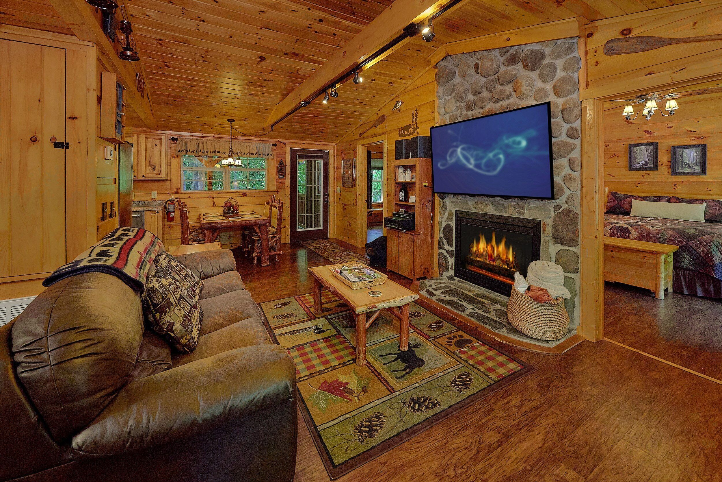 A cozy cabin interior with a stone fireplace, wooden furniture, and a television mounted on the wall.