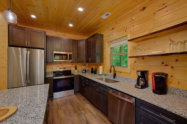 A compact kitchen with wooden walls, stainless steel appliances, and a granite countertop.