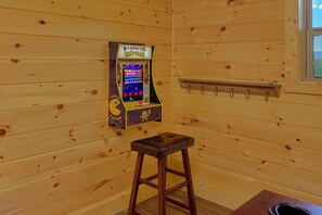 A wooden room with a vintage arcade game, a small stool, and a window.