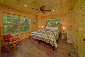 A wooden cabin bedroom with a bed, a rocking chair, and large windows. - Mountain Harmony | Mtn Views, Hot Tub, Game Room, King Suites, Fire Pit + Free Attraction Tickets (Gatlinburg)