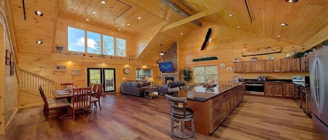A spacious log cabin interior with a large dining area, a living room, and a kitchen.
