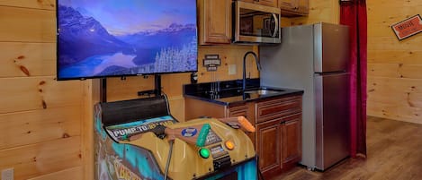 A room with a television displaying a game, a kitchen area, and a sign indicating a movie theater.