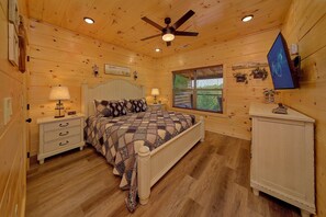 Ein Schlafzimmer einer Holzhütte mit einem Bett, Nachttischen, einem Deckenventilator und einem Fenster mit Jalousien.