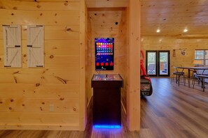 Ein Holzkamin mit einem Retro-Arcade-Automaten, einem Tisch mit Stühlen und einer Tür, die nach draußen führt.