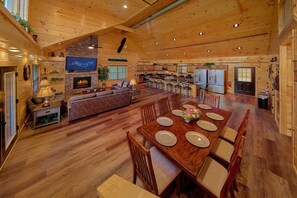 A spacious living area with a fireplace, a television, and a dining table set for six. - An Eagle's View 6 Bedroom Cabin Rental (Pigeon Forge)